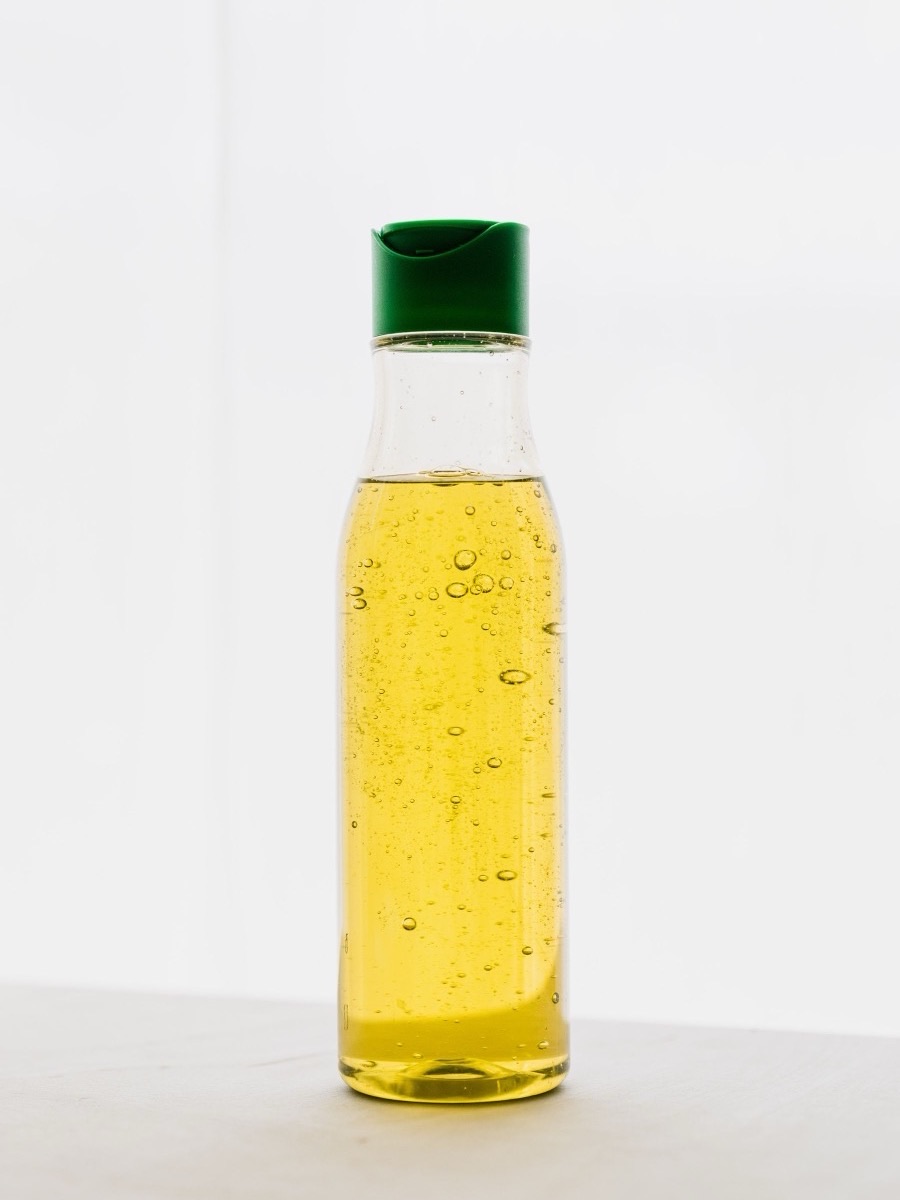 A clear unlabeled plastic bottle with a green flip-top cap holding a pale yellow liquid on a white background