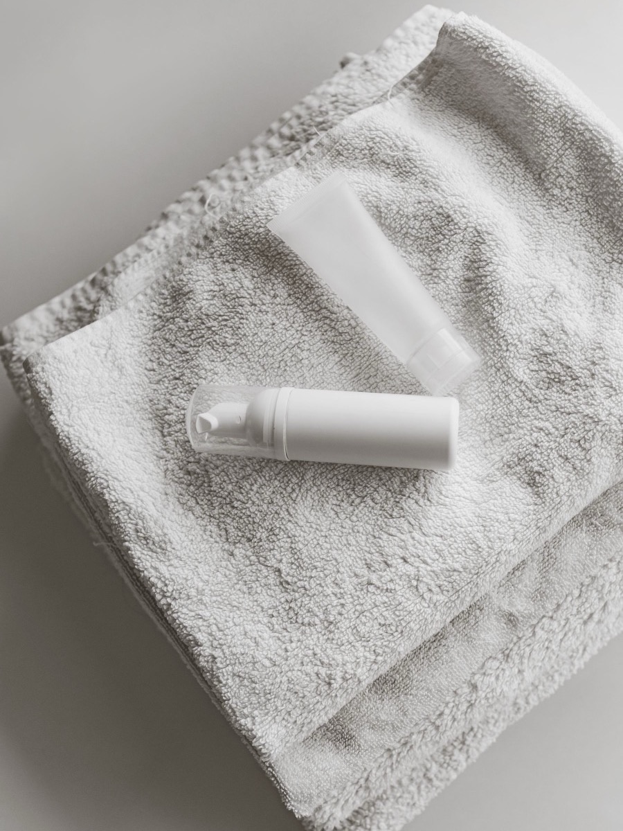 A plain white cream tube and an unlabeled white foam pump bottle on a stack of light gray towels